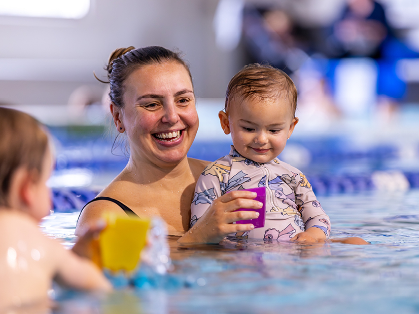 Mum holding their baby as they play in the water together